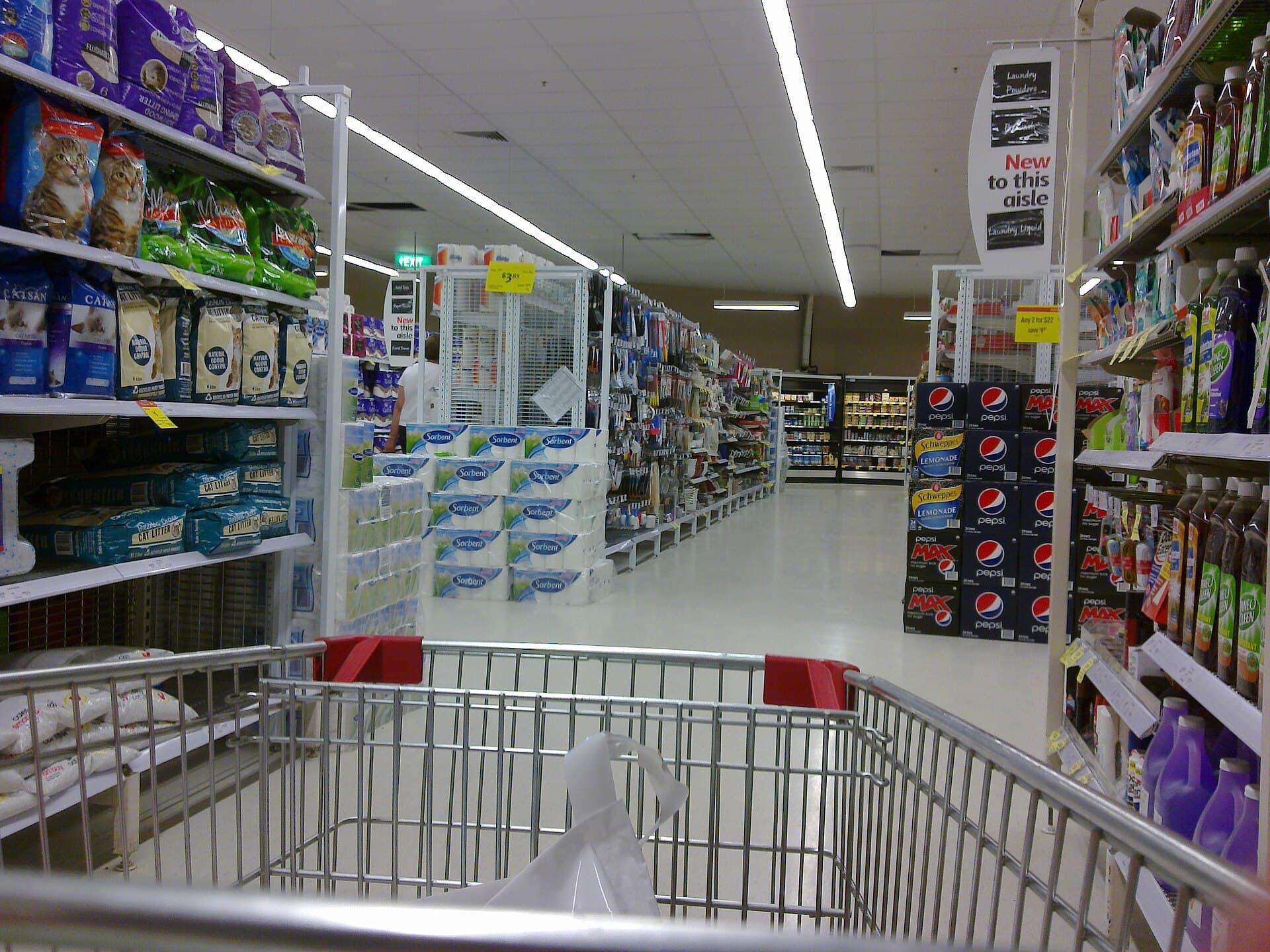 A supermarket aisle with stocked shelves receding under bright store lighting.